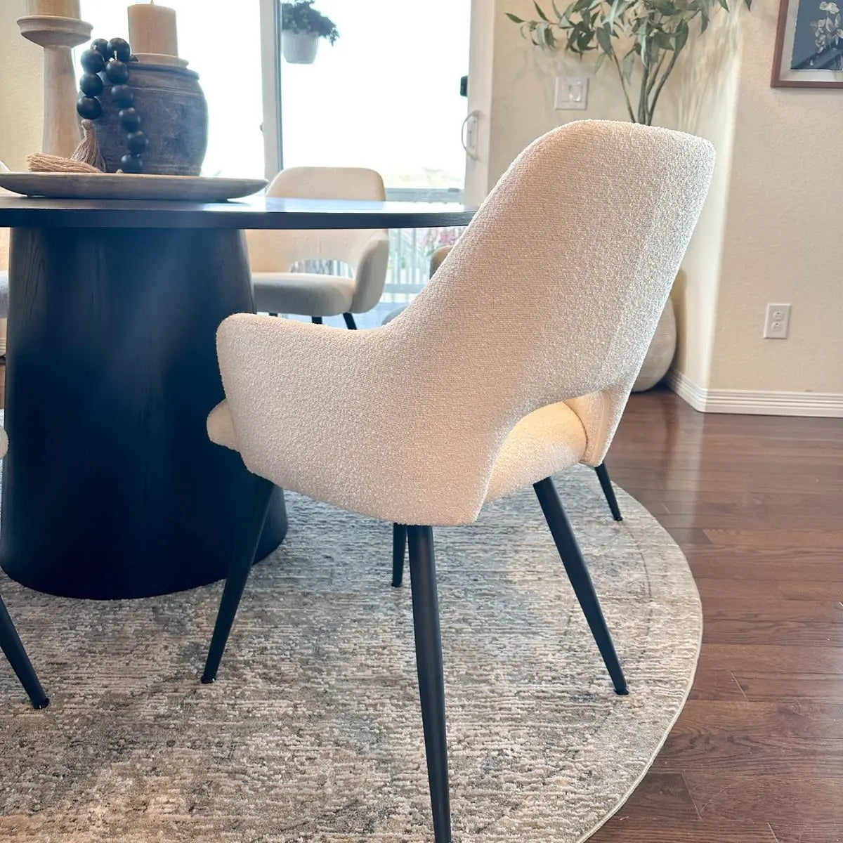Edwin dining chair upholstered with arms near dark table, wooden floor, beige rug, and decor.