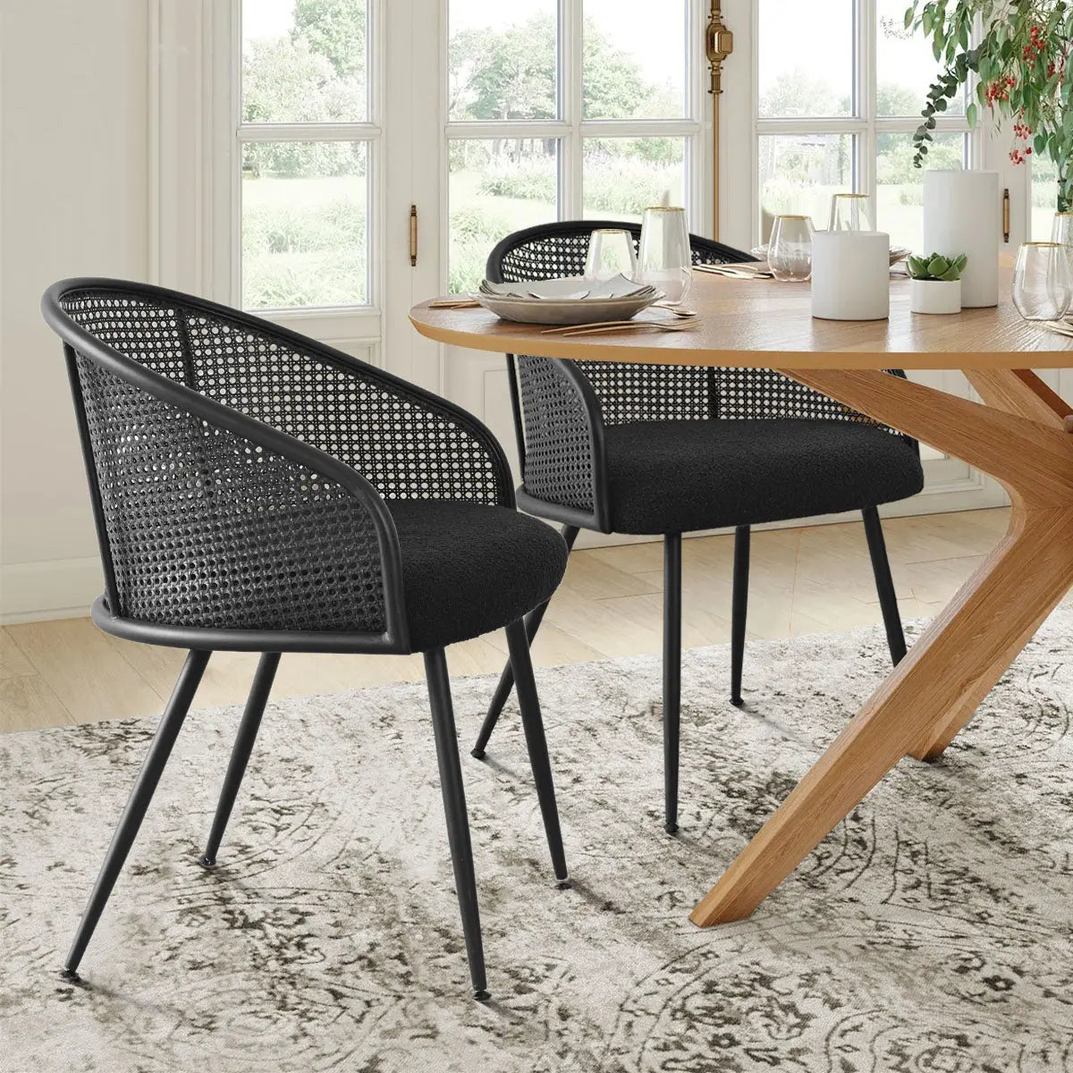 Jules Modern Upholstered Rattan Dining Chair with Arms, wooden dining table, patterned rug, window view.