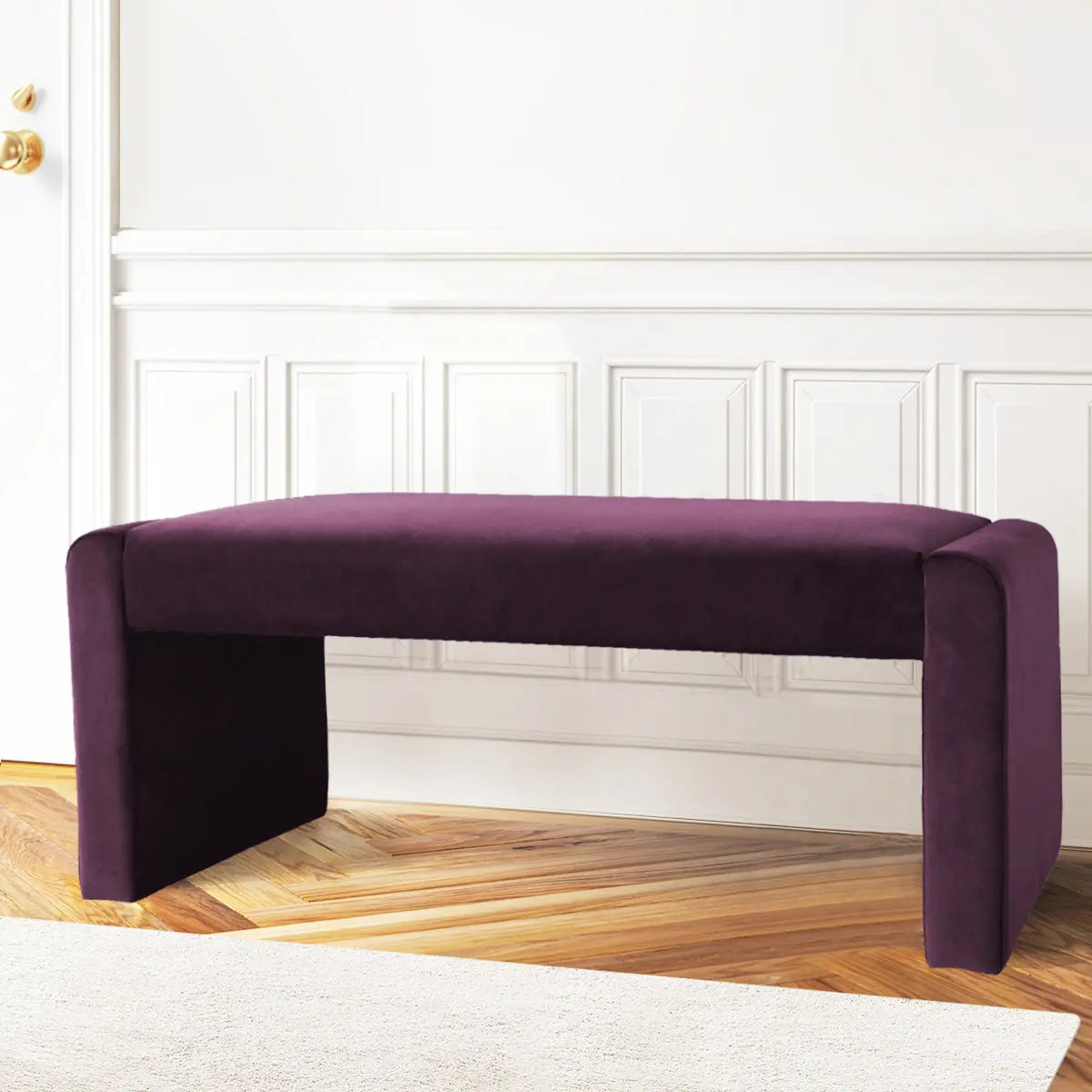 Kaia Modern Leather & Velvet Waterfall Bench in purple, white paneled wall, wooden chevron flooring.