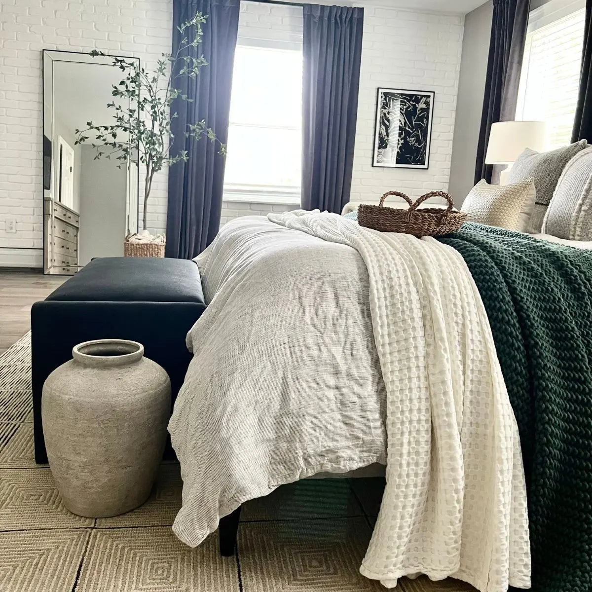 Kaia Waterfall Bench in modern bedroom with white brick walls, gray curtains, and wooden flooring.