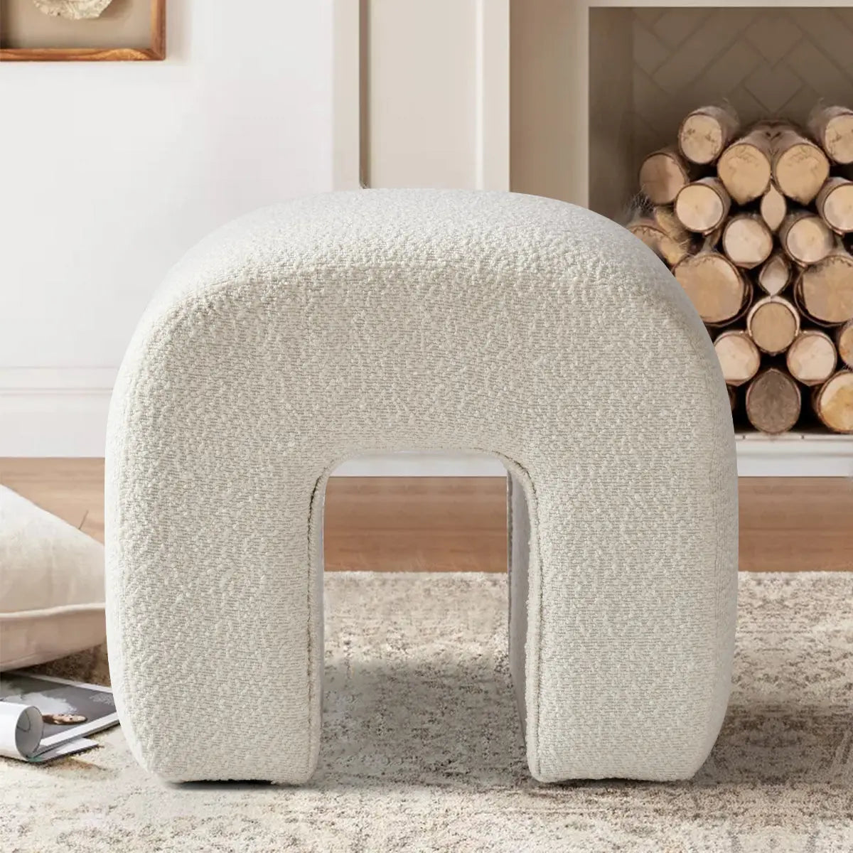 Lily Beige Boucle Waterfall Ottoman beside fireplace on rug with wood flooring in cozy living room.