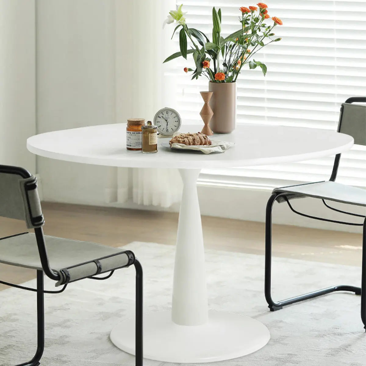 Haven Modern White Round Dining Table with black chairs, light wood flooring, and window blinds.