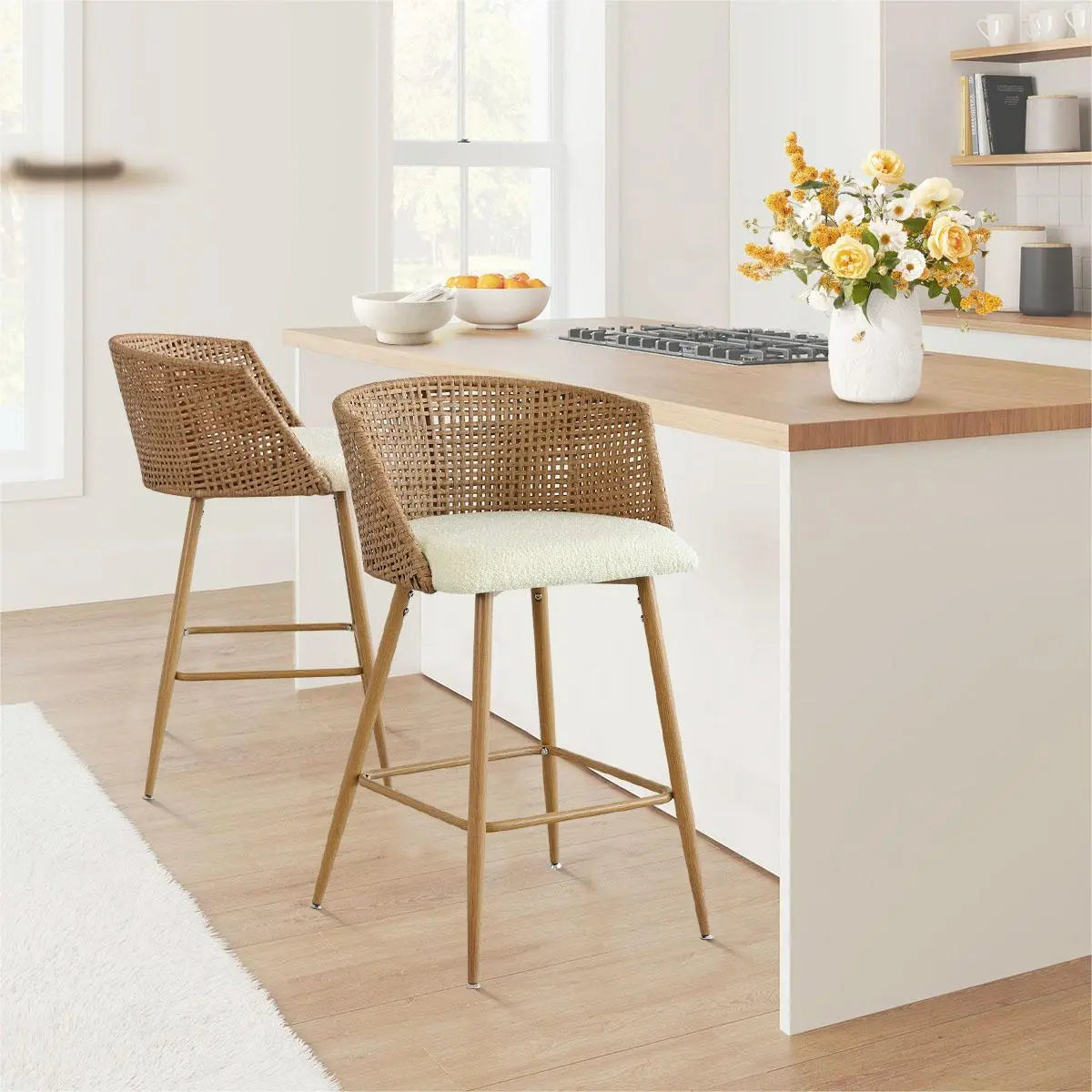 Beige rattan curved-back counter stools in kitchen with light wood flooring and white wall.