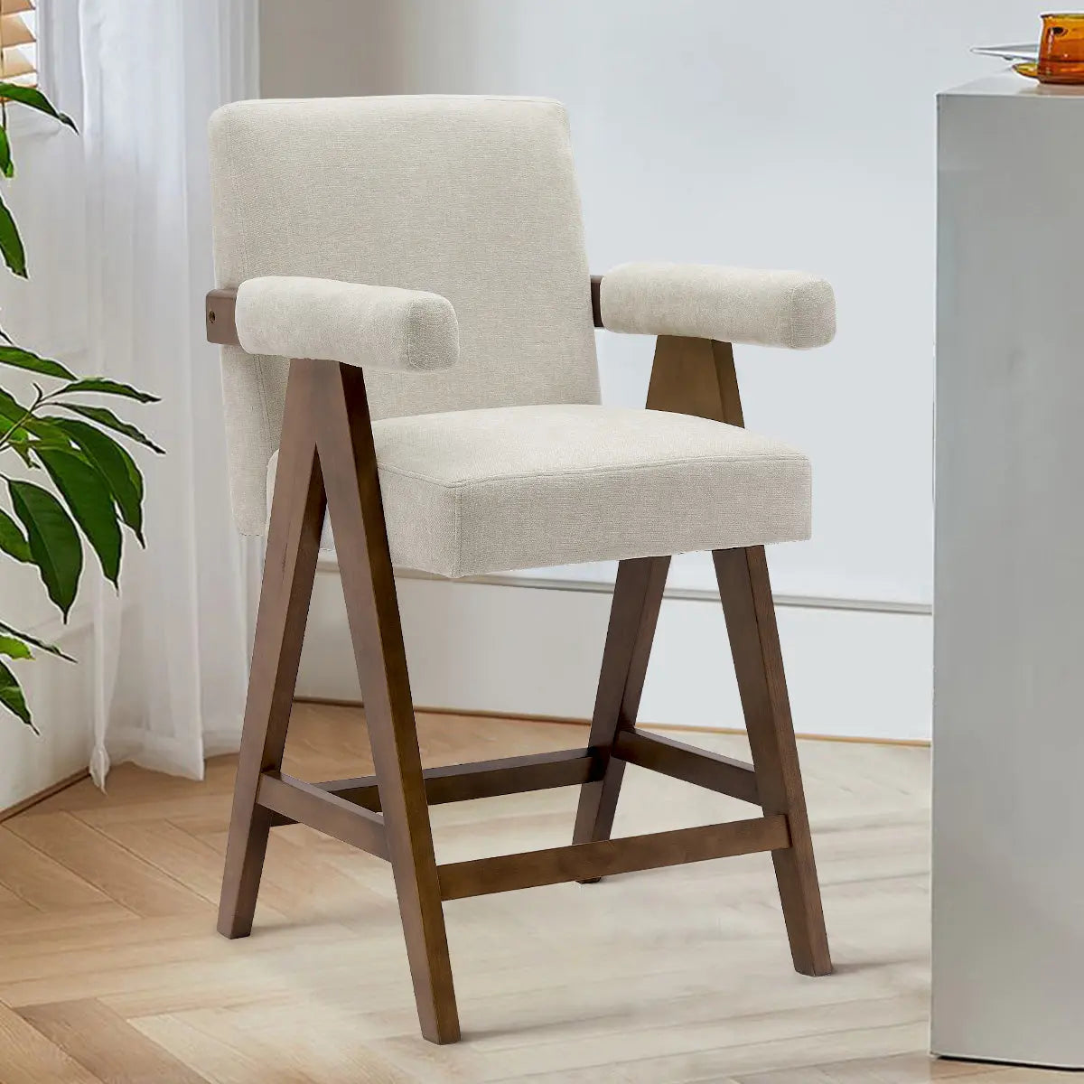 Mid-Century Modern Counter Stool, beige upholstery, wooden legs, light wood flooring, visible foliage.