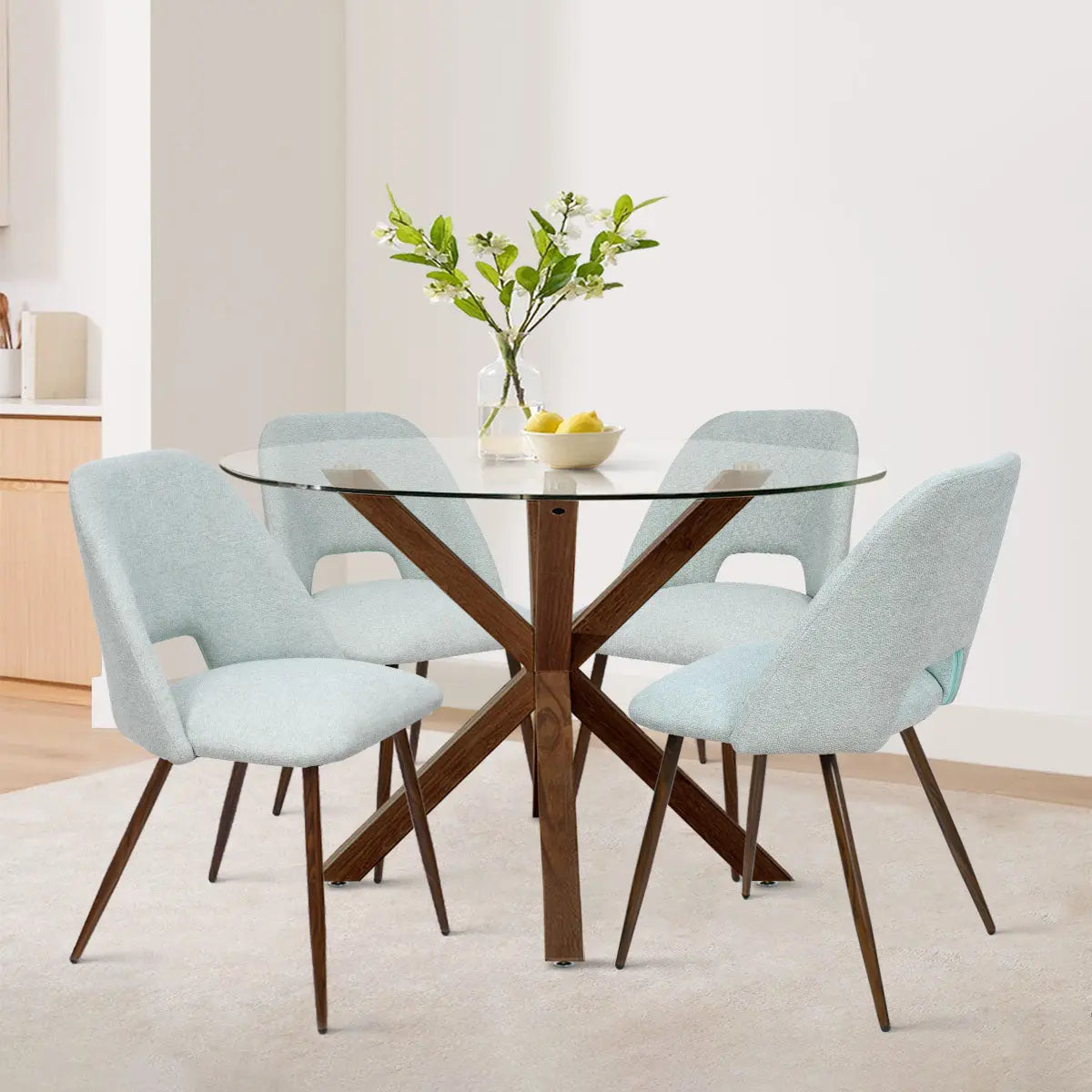 Oliver & Edwin round glass top dining table set with blue chairs, white walls, wooden flooring.