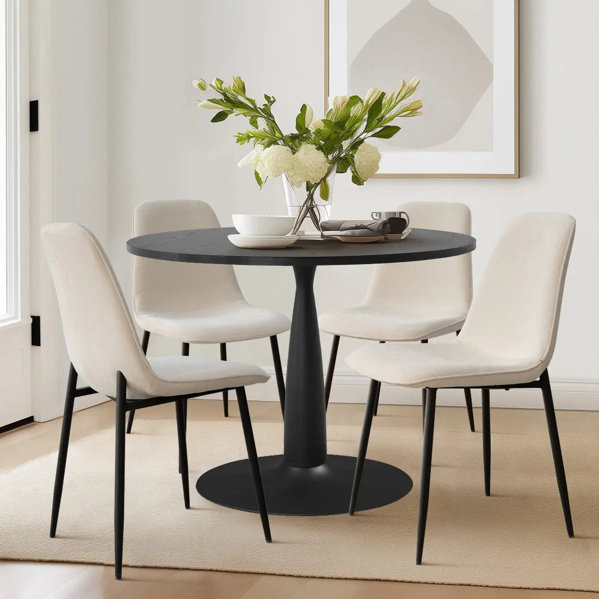 Haven & Oslo dining table set with black round table, four beige chairs, light wood flooring.