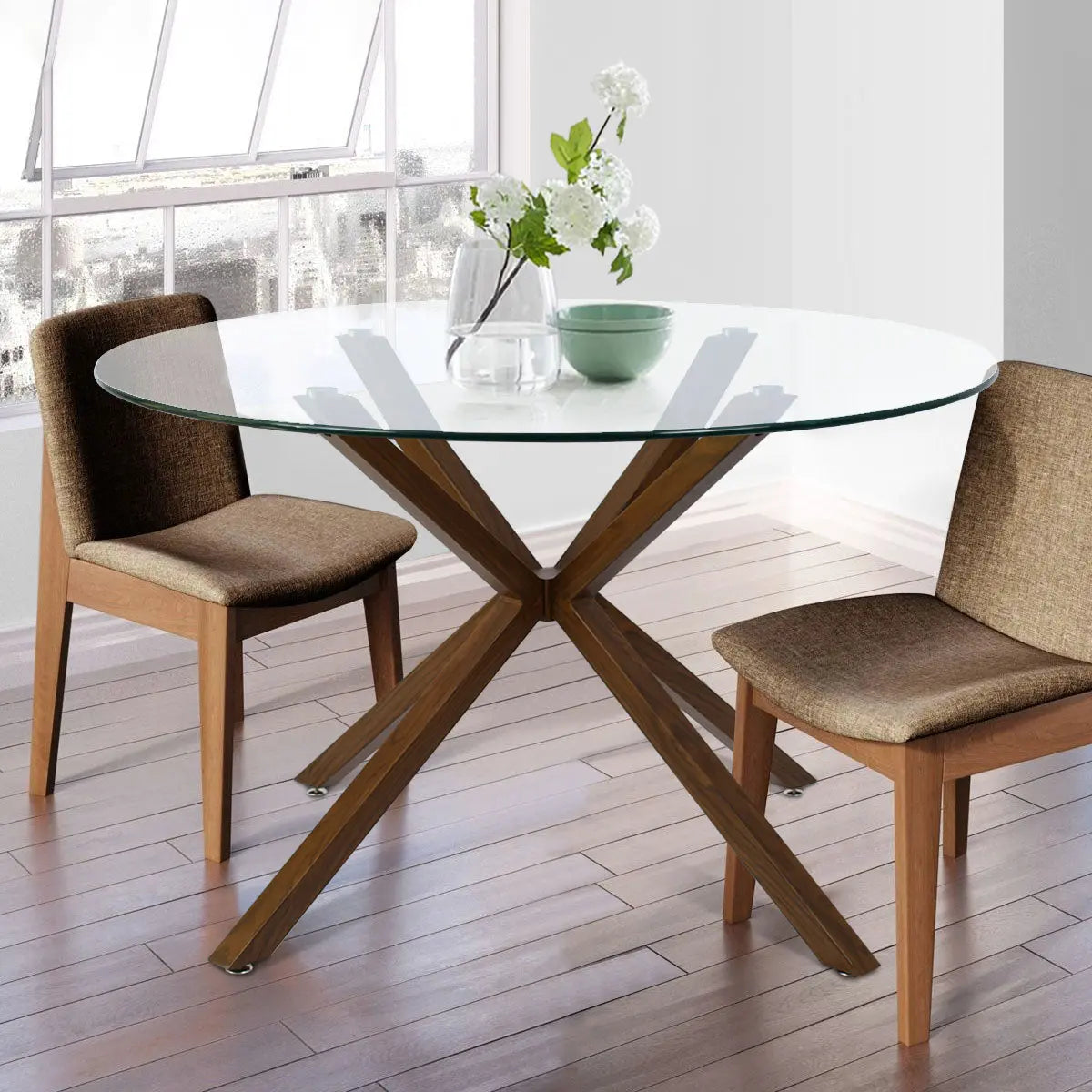 Oliver Modern Glass Dining Table with wooden legs, brown chairs, light wood flooring, white walls.